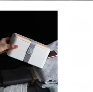 Detail view of a double-layer lunch box with wood-textured lid and grey elastic strap