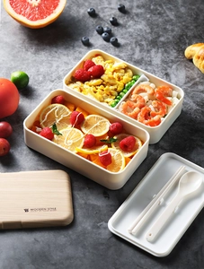 Close-up of a cream double-layer bento box with wooden lid and matching utensils on dark desk