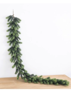 Close-up of artificial green pine needle garland hanging on a white wall over a wooden table