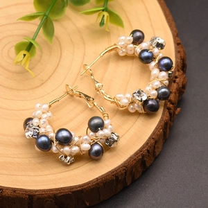 Dettaglio di orecchini a cerchio in filo dorato con perle naturali e strass