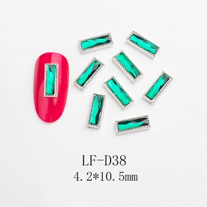 Macro view of emerald green rectangular nail art rhinestones with silver metal borders