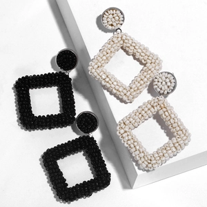 Detail of handmade geometric beaded drop earrings with black and cream white square patterns