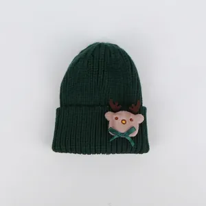 Dettaglio del berretto in maglia verde scuro con renna rosa di peluche e fiocco