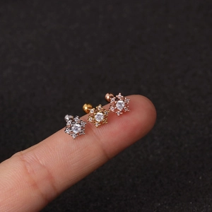 Macro detail of three snowflake cartilage studs in silver, gold, and rose gold finishes