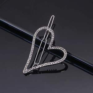 Close-up of a silver heart-shaped hair clip with shimmering rhinestones on a sleek surface