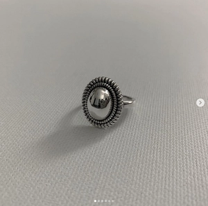 Macro shot of silver retro oval mirror ring with detailed rope texture on gray canvas