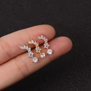 Three dainty zircon flower ear studs in silver, gold, and rose gold on a finger