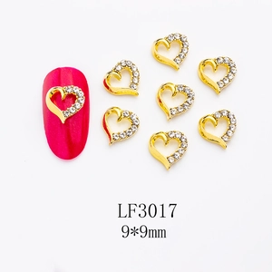 Macro detail of gold alloy heart nail charms with rhinestones sized 9x9mm on red nail