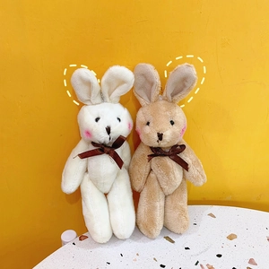 Close-up of soft white and brown plush bunny pendants with silk bows on yellow backdrop