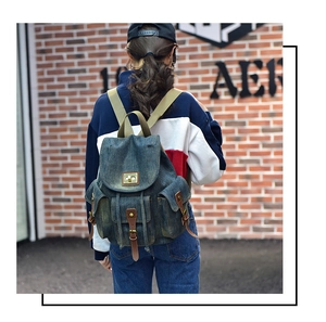 Dettaglio dello zaino vintage in denim con cinturini in pelle marrone e fibbie su muro di mattoni