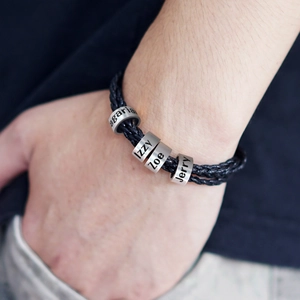 Gros plan d'un bracelet en cuir tressé noir avec quatre perles personnalisées gravées