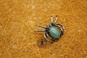 Macro shot of a vintage silver spider brooch featuring a polished green gemstone center