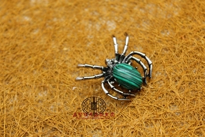 Detailed view of a silver spider brooch with a green malachite stone inlay on rustic straw
