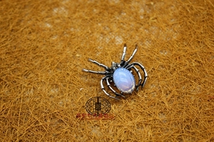 Macro detail of a silver spider brooch featuring an oval blue sandstone inlay on straw