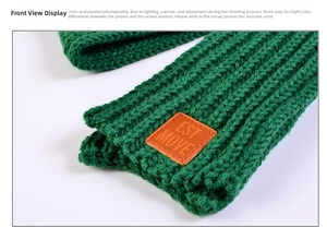 Detail of green knit scarf featuring thick texture and a brown leather EST MOVE label