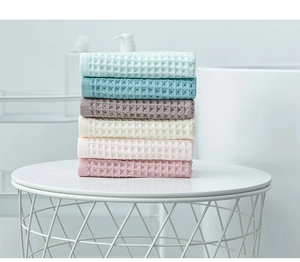 Stack of colorful waffle weave cotton towels in soft pastel tones on a minimalist metal table
