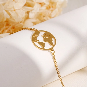 Elegant gold world map pendant bracelet made of stainless steel on white prop with flowers
