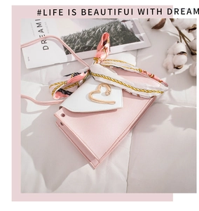 Detail of pink leather crossbody bag with heart buckle and elegant striped silk scarf accent