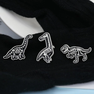 Detailed close-up of three black and white dinosaur skeleton enamel pins on fabric