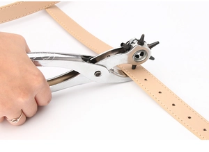Close-up of a rotating metal leather hole punch tool making a hole in a beige belt