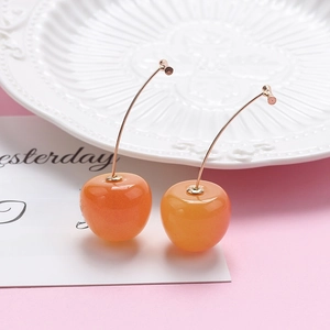 Detail view of cute orange cherry dangle earrings with a glossy gradient finish on a dish