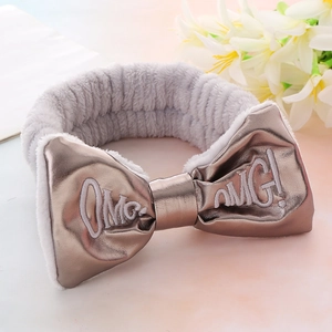 Close-up of grey plush headband featuring 'OMG!' embroidery and a metallic bow detail