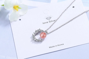 Close-up of crescent moon necklace with strawberry quartz stone on card