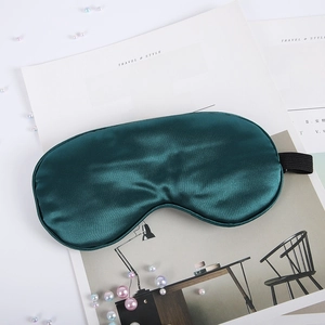 Detail of dark green silk sleep mask with satin finish on minimalist magazine background