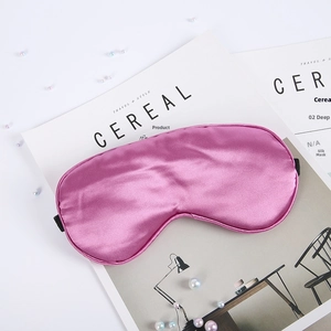 Pink faux silk sleep mask detail with elastic strap and pearl decoration on a magazine