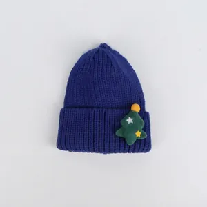 Dettaglio del berretto natalizio in maglia blu navy con patch albero e pompon gialli