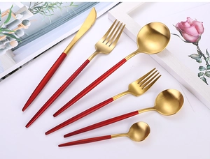 Dettaglio di eleganti posate in acciaio inossidabile oro e rosso su sfondo bianco