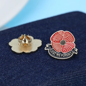 Detailed view of red enamel poppy brooch with Lest We Forget ribbon on denim fabric