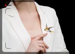 Detail of colorful enamel swallow brooch on white blazer collar with flying bird design