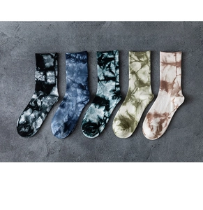 Chaussettes en coton tie-dye en cinq couleurs posées à plat sur un fond en ciment texturé