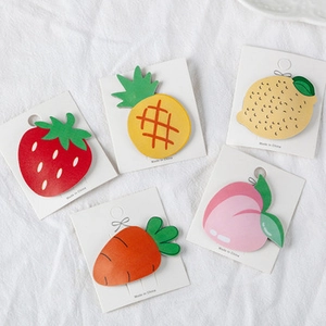 Macro view of five fruit and vegetable hair clips on a white linen display board