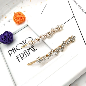 Détail de barrettes dorées avec perles et strass brillants posées sur un cadre photo