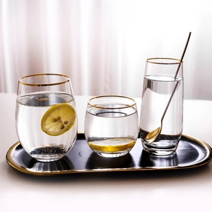 Elegant egg-shaped glass set with gold rim and lemon water on a black oval tray