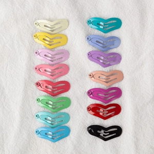 Top view of sixteen colorful heart-shaped metal snap hair clips on white textured fabric