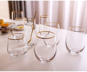 Close-up of glass tumblers with gold rims and dried lemon slices on a white table