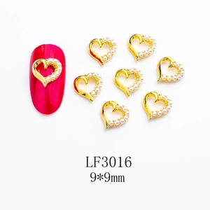 Detail of heart-shaped alloy nail charms with pearls and 9x9mm dimensions on red nail