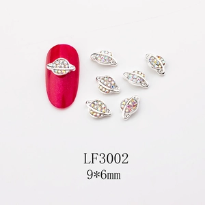 Macro shot of 9x6mm silver Saturn nail charms with AB rhinestones on a red nail sample