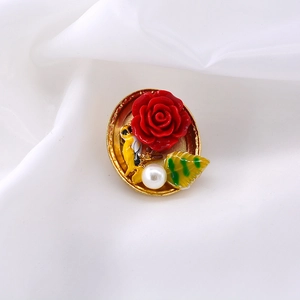 Detailed close-up of a gold baroque brooch featuring a red rose, bird, and white pearl