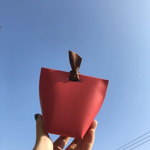 Minimalist red paper gift box with brown ribbon knot held against a clear blue sky