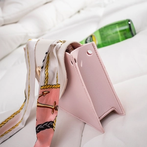 Pink leather handbag with triangle side profile and printed silk scarf on soft white bedding