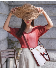 Outdoor shot of white floral handbag with red straps and woven straw hat detail
