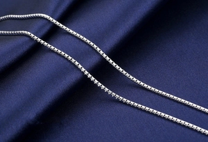 Macro shot of silver box chain necklace on blue silk fabric showing fine metal texture