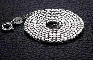 Macro shot of a polished silver box chain necklace coiled on a black leather background