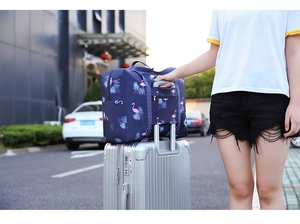 Waterproof travel bag with flamingo print slipping over a silver suitcase handle