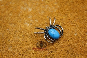 Macro detail of silver spider brooch with oval blue stone and intricate metal legs