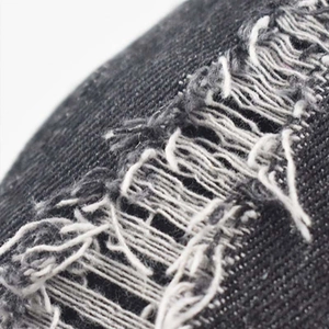 Close-up of distressed black denim baseball cap fabric with ripped texture and white threads